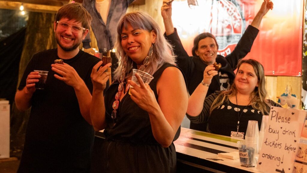 People holding drinks and smiling at a bar. Behind the bar are two staff members, also smiling.